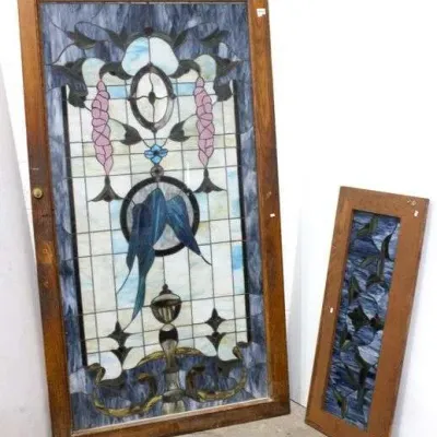 Two antique stained glass windows in wooden frames, featuring intricate floral and bird motifs in shades of blue, pink, and white.