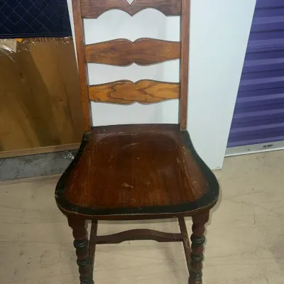 Sale Photo Thumbnail #58: Vintage wooden ladder-back side chair featuring a decorative carved top rail, turned front legs, and a dark-stained seat with a painted black border.
