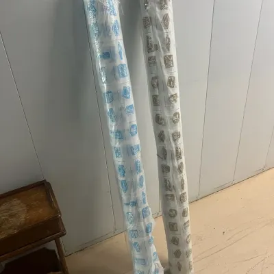 Sale Photo Thumbnail #32: Two rolls of vintage patterned paper or vinyl wrap, one with blue illustrations and one with brown illustrations, both sealed in protective plastic.