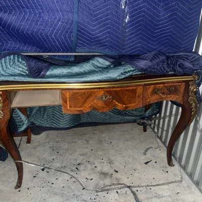 Sale Photo Thumbnail #65: French Provincial style writing desk with inlaid wood veneer, ornate brass hardware, and cabriole legs featuring gilt metal mounts, shown partially covered by moving blankets.