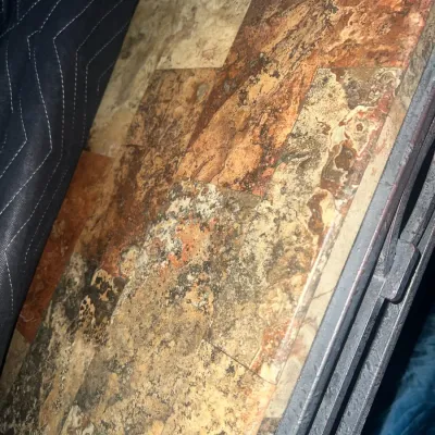 Sale Photo Thumbnail #77: Close-up of a table surface featuring a rustic slate tile inlay in warm earth tones, bordered by a dark metal frame.