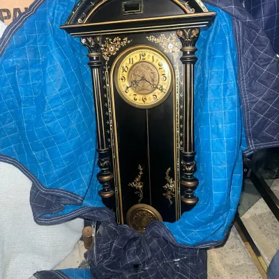 Sale Photo Thumbnail #48: Antique black-lacquered wall clock featuring ornate gold-painted floral details, fluted columns, and mother-of-pearl inlay, partially wrapped in a blue moving blanket.