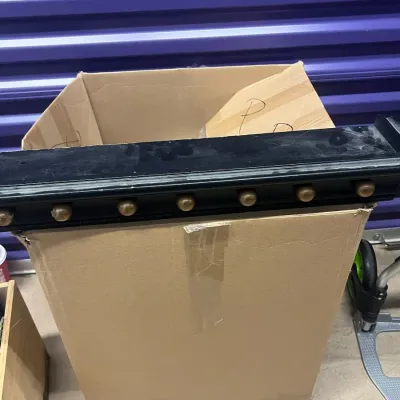 Sale Photo Thumbnail #74: Black wooden coat rack with brass pegs, resting on a cardboard box in a storage unit.