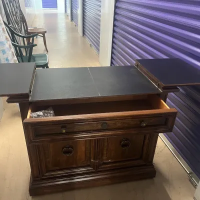 Sale Photo Thumbnail #40: Vintage wooden bar cabinet with a fold-out black laminate top, featuring a single drawer and lower cabinet doors with ring pulls.