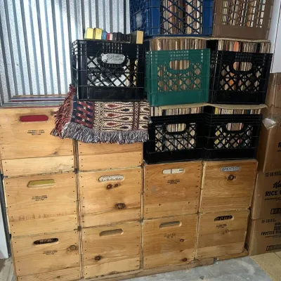 Sale Photo Thumbnail #2: Large collection of vinyl records stored in plastic milk crates and stacked wooden storage boxes.