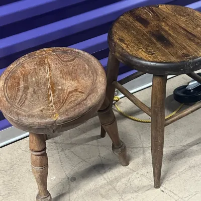 Sale Photo Thumbnail #94: Two vintage wooden stools, one with a lighter, weathered finish and turned legs, and the other with a darker, polished seat and tapered legs.