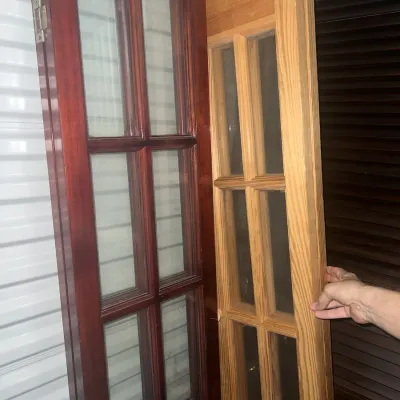 Sale Photo Thumbnail #52: Two wooden French doors with glass panes, one in a dark cherry finish and the other in a light natural oak finish.