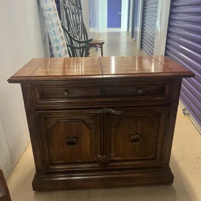 Sale Photo Thumbnail #26: Traditional dark wood bar cabinet or server with a split-top design, a single drawer, and two lower cabinet doors featuring ornate metal ring pulls.