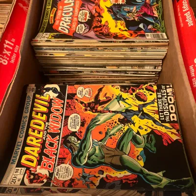 Sale Photo Thumbnail #97: Stacks of vintage Marvel comic books in a cardboard box, featuring Daredevil #98 (April 1973) and The Tomb of Dracula #64 (May 1978).