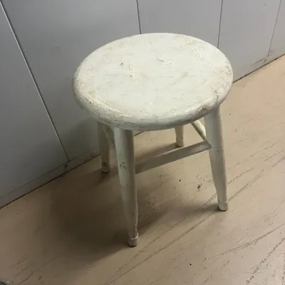 Sale Photo Thumbnail #31: Vintage white-painted wooden stool with a round seat and four splayed legs, showing significant wear and distressing.