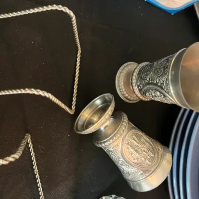 Two vintage pewter or silver-plated goblets featuring ornate embossed relief designs, shown alongside a twisted metal stand and other...