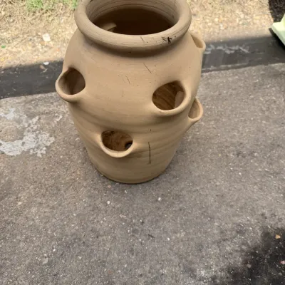 Terracotta strawberry planter pot with multiple side pockets, showing minor surface wear and dirt from outdoor use.