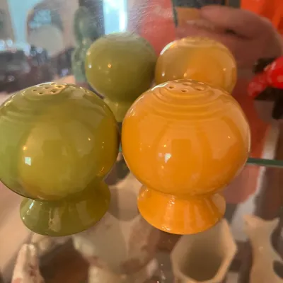 Vintage Fiesta ceramic salt and pepper shakers in olive green and butterscotch yellow, displayed on a glass shelf.