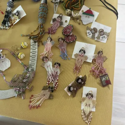 Collection of handmade beaded jewelry and ornaments, featuring several angel-shaped beaded earrings and pins alongside various necklaces...