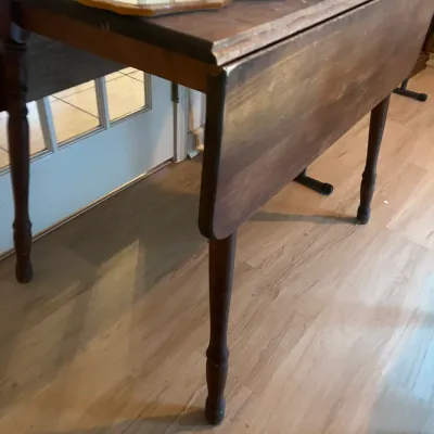 Vintage wooden drop-leaf table with turned legs, showing some wear to the finish, topped with various vanity items.