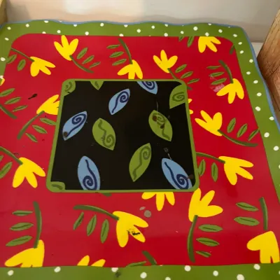Whimsical square ceramic serving platter featuring a vibrant red background with yellow flowers, a green polka dot border, and a central...