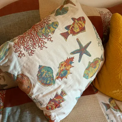 Square throw pillow featuring a colorful embroidered marine life motif with fish, starfish, shells, and coral on an off-white background.