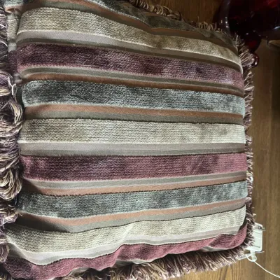 Square decorative throw pillow featuring a striped pattern in shades of sage green, mauve, and beige, finished with a thick fringe trim.