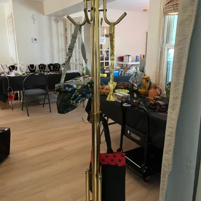 Vintage brass coat rack with multiple hooks, shown holding a patterned bag and a tote, with various estate sale items displayed on tables...