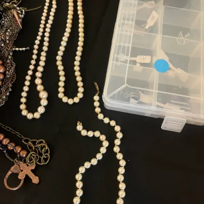 Assorted costume jewelry including several faux pearl necklaces, a chunky chain necklace with a cross pendant, and a clear plastic...