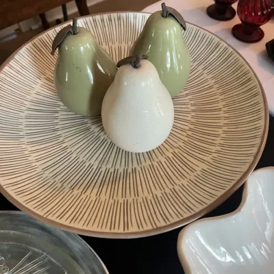Three ceramic decorative pears in shades of green and white, displayed on a large ceramic platter with a radiating brown line pattern.