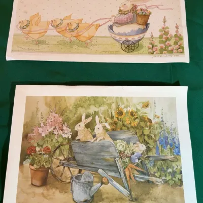 Two unframed Easter-themed art prints by Sandi Gore Evans, featuring whimsical illustrations of rabbits, chicks, and garden scenes.