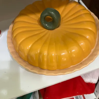 Vintage ceramic pumpkin-shaped covered serving dish with a green stem handle, resting on a matching scalloped base.