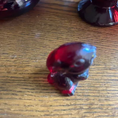 Vintage ruby red glass bird figurine, shown alongside other ruby glass pieces on a wooden surface.