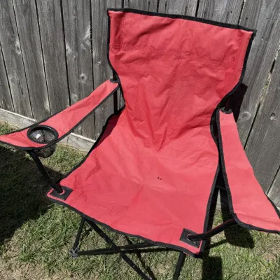 Red folding camp chair with a built-in mesh cup holder on the armrest, showing minor wear.