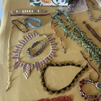 Assortment of handmade beaded necklaces and bracelets in various colors, styles, and patterns, displayed on a yellow tablecloth.