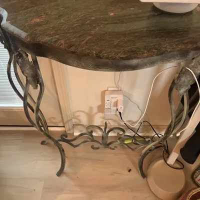 Ornate wrought iron console table featuring a contoured green marble top and decorative scrollwork legs.