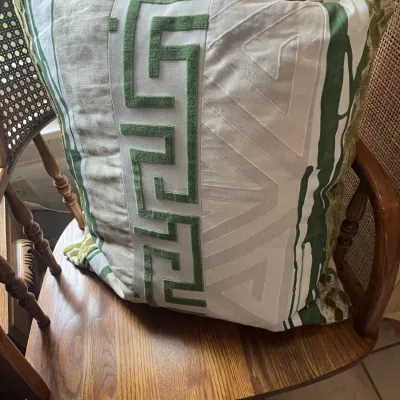 Large decorative throw pillow featuring green Greek key velvet trim and geometric embroidered patterns, resting on a vintage wooden...