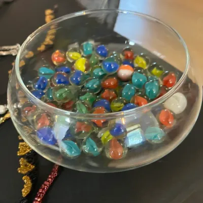 Clear glass fishbowl-style container filled with an assortment of colorful vintage cat's eye marbles.