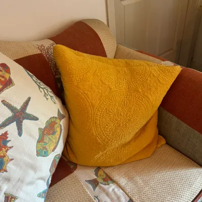 Bright yellow quilted throw pillow with a circular mandala pattern, resting on a patchwork sofa with coastal-themed fabric panels.