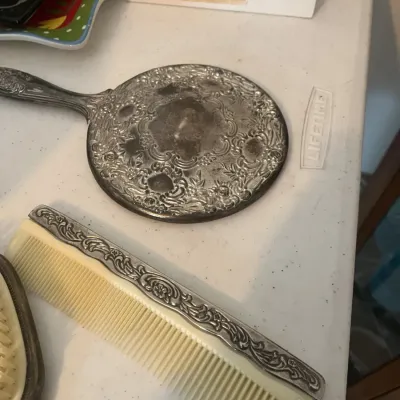 Vintage silver-plated vanity set pieces, including an ornate floral-embossed hand mirror and a matching comb with a silver-toned...