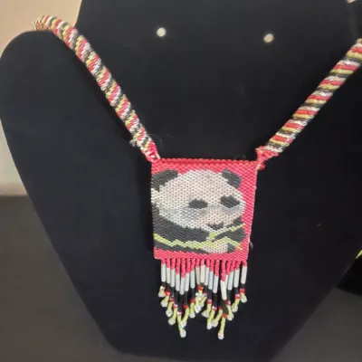 Hand-woven beaded necklace featuring a panda bear motif on a pink background, complete with a matching beaded strap and hanging fringe...