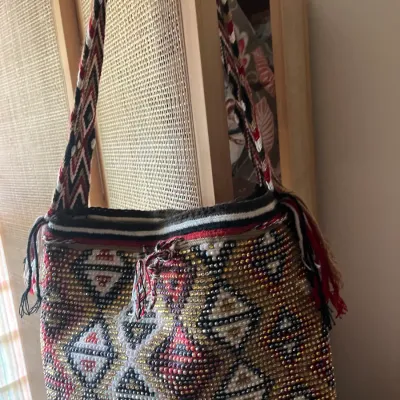 Handwoven Wayuu mochila shoulder bag featuring intricate geometric patterns, beaded embellishments, and a wide woven strap.