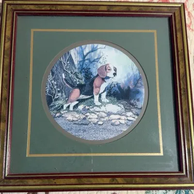 Framed circular print of a beagle puppy by a stream, set in a green mat with a gold border and housed in a wood-grain frame.