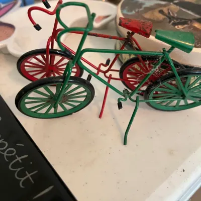 Pair of vintage miniature wire bicycle figurines in red and green, showing some wear and light rust.