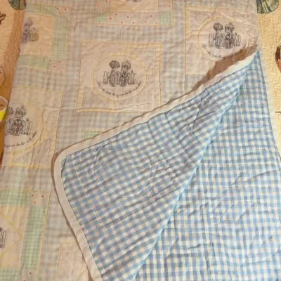 Vintage Precious Moments baby quilt featuring a patchwork design with illustrated panels and a blue-and-white gingham reverse side.