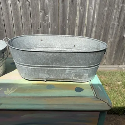 Vintage galvanized metal oval wash tub with side handles, showing minor wear and weathering.
