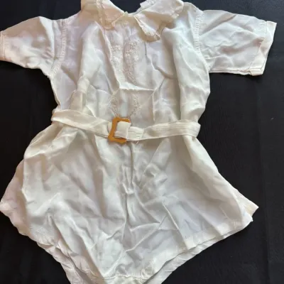 Vintage white baby romper featuring a lace-trimmed collar, embroidered chest detail, and a matching belt with a yellow buckle.