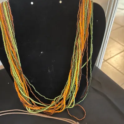 Multi-strand seed bead necklace in shades of green, orange, and brown, displayed on a black velvet bust.