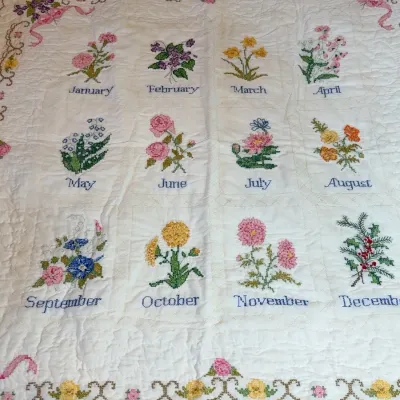 Vintage hand-embroidered calendar quilt featuring floral motifs for each month of the year on a white quilted background.