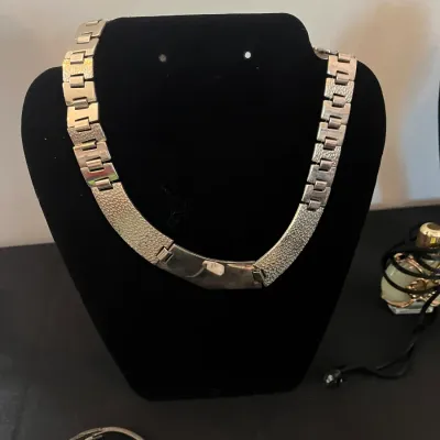 Vintage silver-tone collar necklace featuring textured panels and a link chain, displayed on a black velvet bust.
