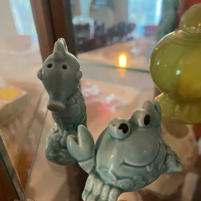 Vintage light blue ceramic seahorse and crab salt and pepper shakers, displayed on a glass shelf.