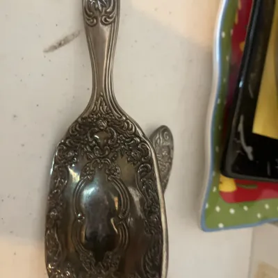 Vintage silver-plated hairbrush featuring an ornate repoussé floral and scrollwork pattern on the back and handle.