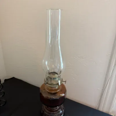 Vintage amber glass oil lamp featuring a tall, clear glass chimney and an ornate embossed base.