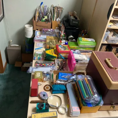 Large assortment of art, craft, and drafting supplies spread across a light-colored table, including colored pencils, Crayola crayons,...