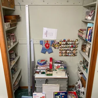 Craft and sewing closet filled with various supplies, including thread racks, storage carts, photo paper, rulers, and notions.